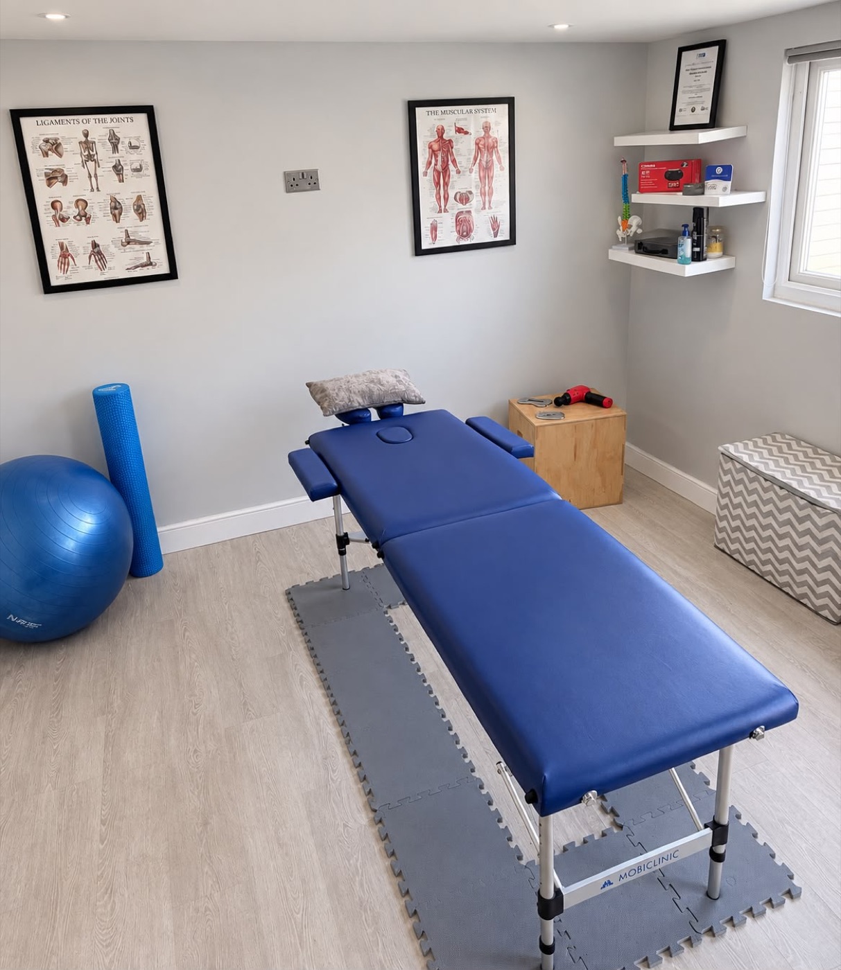 The Phull Motion treatment room in Bexleyheath, with a blue treatment table, anatomy posters and a Theragun